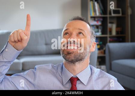Un homme heureux qui pointe vers le haut. Homme barbu portant une chemise de travail. Homme de race blanche adulte en 30s ou 40s. Doigt vers le haut. Banque D'Images