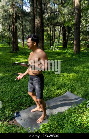 Des yogi masculins actifs et beaux se promène dans un parc en forêt avant ou après un entraînement. Jeune homme sportif hispanique, cours de yoga avec tapis de fitness Banque D'Images