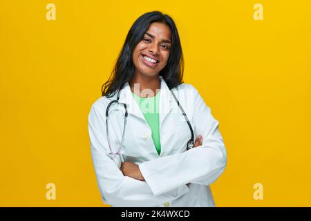 Jeune femme gaie médecin debout par un fond jaune souriant regardant caméra, Indien isolé Banque D'Images