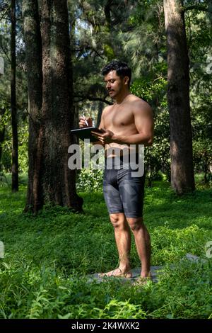 Des yogi masculins actifs et beaux se promène dans un parc en forêt avant ou après un entraînement. Jeune homme sportif hispanique, cours de yoga avec tapis de fitness Banque D'Images