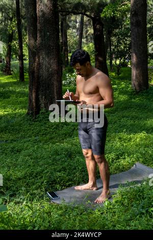 Des yogi masculins actifs et beaux se promène dans un parc en forêt avant ou après un entraînement. Jeune homme sportif hispanique, cours de yoga avec tapis de fitness Banque D'Images