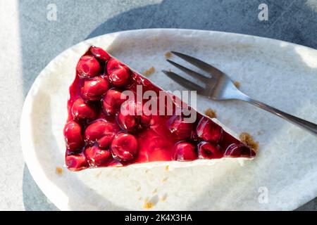 Une vue de dessus d'une seule tranche ou d'une portion de gâteau au fromage de cerise fraîchement préparé. Il est servi sur une assiette sur une table extérieure dans un café. Banque D'Images