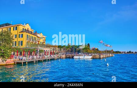 La jetée avec des drapeaux, des restaurants en plein air et des hôtels pittoresques du lac de Garde, Sirmione, Italie Banque D'Images