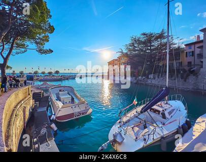 Le magnifique coucher de soleil doré sur la petite marina de Sirmione avec des bateaux de pêche et de tourisme à bascule contre des maisons colorées et le lac de Garde, en Italie Banque D'Images