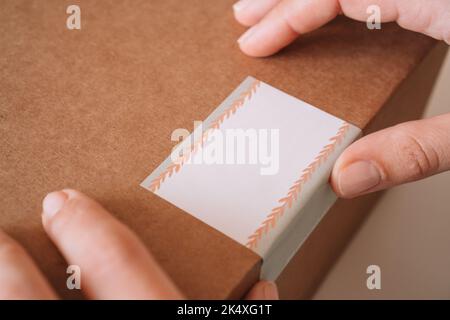 Photo rognée des mains de femmes emballage, préparation avec bande scotch, colis pour livraison à l'acheteur. La femme colle l'autocollant à la boîte en carton kraft Banque D'Images