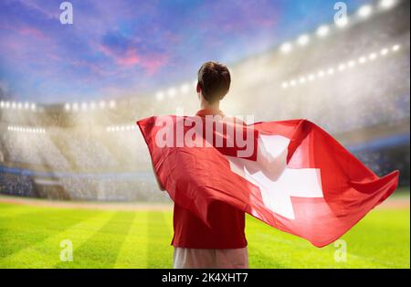 Suisse supporter de football sur le stade. Fan suisse sur le terrain de football en regardant jouer l'équipe. Jeune joueur avec drapeau et maillot national Banque D'Images