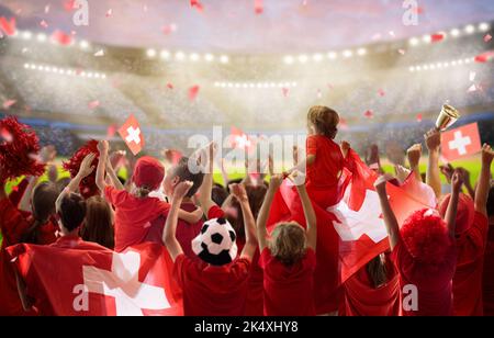 Suisse supporter de football sur le stade. Fan suisse sur le terrain de football en regardant jouer l'équipe. Groupe de supporters suisses avec drapeau et maillot national Banque D'Images