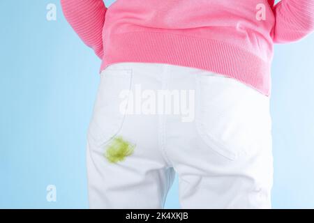 Taches d'herbe sur le Jean.la fille debout avec une tache d'herbe sale sur le pantalon blanc avec son dos tourné sur un fond bleu. Isolé. Vêtements gâtés. Banque D'Images