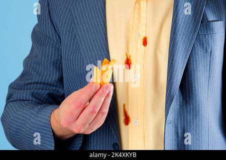 Frites dans la main d'un homme sur fond de taches de ketchup sur une chemise jaune. Isolé sur fond bleu Banque D'Images