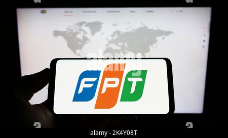 Personne tenant un téléphone portable avec le logo de la société INFORMATIQUE vietnamienne FPT Corporation à l'écran devant la page Web des affaires. Mise au point sur l'affichage du téléphone. Banque D'Images