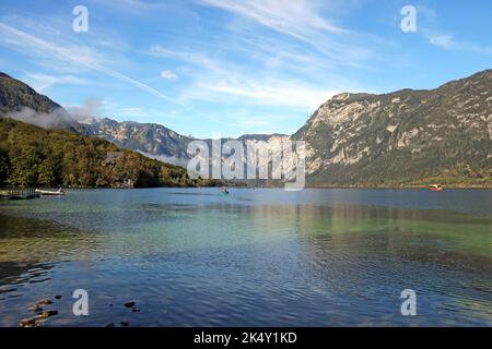 Lac de Bohinj en Slovénie avec des gens sur des canoës et des montagnes avec un ciel bleu ciel nuageux en arrière-plan. Banque D'Images