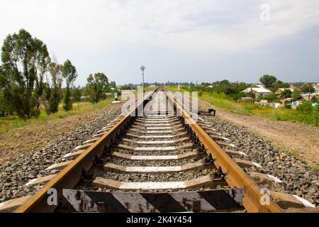 Chemin de fer à l'horizon. Rails de chemin de fer et traverses en béton en toile de fond d'une zone rurale avec des maisons d'un étage, des arbres et un ciel bleu Banque D'Images