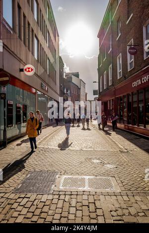 En fin d'après-midi, la lumière du soleil projette des ombres sur les acheteurs et les visiteurs dans les rues animées de la ville de York, dans le Yorkshire, en Angleterre. Banque D'Images