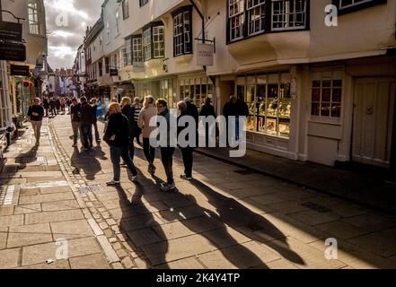 En fin d'après-midi, la lumière du soleil projette des ombres sur les acheteurs et les visiteurs dans les rues animées de la ville de York, dans le Yorkshire, en Angleterre. Banque D'Images