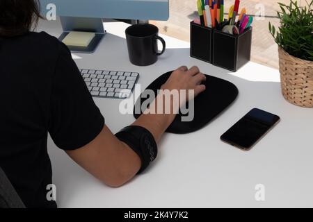 femme méconnue travaillant à l'ordinateur avec tendonitis causé par l'utilisation de souris, portant un coude pour atténuer la douleur Banque D'Images