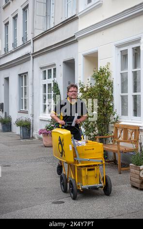 Allemagne, Lübeck - 13 juillet 2022: Gros plan de la voiture jaune de Mailman chatheing dans la rue devant les façades de maisons peintes en blanc Banque D'Images