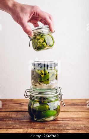 Main mâle tenant l'un des trois jarres en verre de poivrons Jalapeno fraîchement pickés avec des herbes et de l'ail. Copier l'espace Banque D'Images