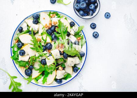 Delicious arugula salad with pears, blueberries, roquefort cheese and walnuts. Black kitchen table background, top view Banque D'Images