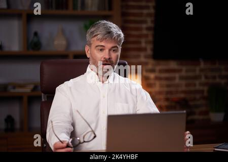 Homme âgé aux cheveux gris travaillant au bureau à domicile avec un ordinateur portable. Portrait d'affaires d'un beau responsable assis sur le lieu de travail. Étudier des cours en ligne Banque D'Images