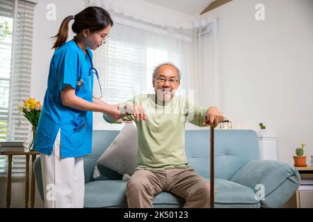 Une jeune femme aide à soutenir les patients orthopédiques pour se lever avec la canne à pied à la maison, une infirmière de soins aide à soutenir l'homme handicapé senior pour se lever avec Banque D'Images