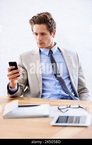 Lecture d'un texte urgent. Un jeune homme d'affaires lisant un message texte de son bureau. Banque D'Images