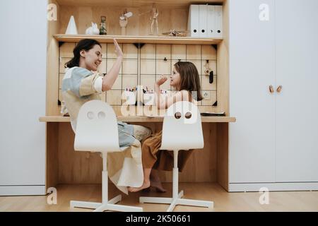 Bonne maman et petite fille mignonne donnant l'autre haut cinq. Ils font leurs devoirs. Assis au bureau. Vue de derrière. Banque D'Images