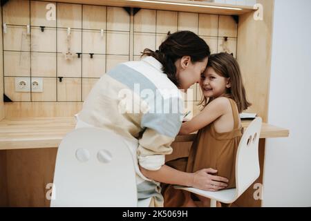 Maman et sa petite fille mignonne touchant les fronts. Ils font leurs devoirs. Assis au bureau. Vue de derrière. Banque D'Images