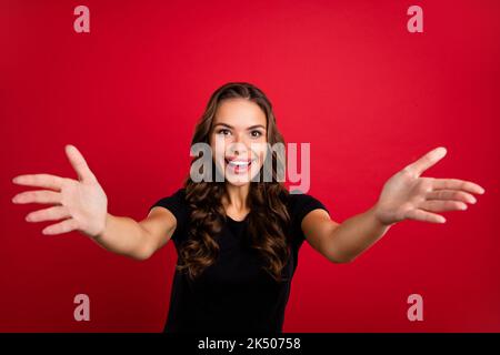 Photo de la jeune femme très impressionnée porter un t-shirt noir à bras ouverts prêt vous embrasser sourire isolé rouge couleur arrière-plan Banque D'Images