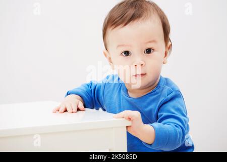 Toujours un peu instable sur mes pieds... Portrait d'un adorable bébé garçon se équilibrant contre une table. Banque D'Images