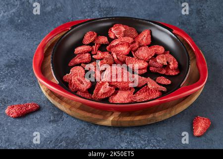 Copeaux de fraise empilés dans une plaque en céramique noire sur un support en bois sur fond de béton gris-bleu. Cent pour cent de fraises naturelles sublimés Banque D'Images