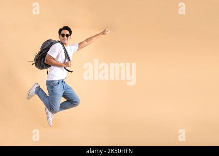 Jeune touriste asiatique routard homme souriant et sautant isolé sur fond beige Banque D'Images