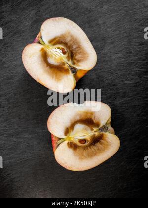 Deux moitiés de l'intérieur d'une pomme coupée ouverte et pourrie, reposant sur le dessus de la planche à découper foncée. Banque D'Images