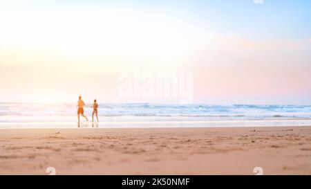 Couple courant sur la plage. Un couple heureux va nager dans l'océan au coucher du soleil. Arrière-plan de vacances d'été flou. Un homme et une femme défocused courent sur une plage de sable. L'été. Des gens heureux Banque D'Images