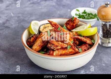 Ailes de poulet Air Fryer sur un bol avec citron garni de marjolaine Banque D'Images