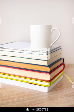 Pile de livres de couverture rigide avec une tasse de café blanc sur le dessus. Banque D'Images