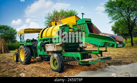 15 août 2022, Sikar, Inde. Cultivateur industriel travaillant dans une terre agricole avec John tracteur et fourrager Thescher dans un champ de mil ou de Pennisetum glaucum. Banque D'Images