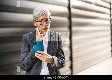 Portrait extérieur d'une femme d'affaires senior qui discute sur un smartphone. Elle est en colère. Banque D'Images