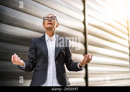 Portrait extérieur d'une femme d'affaires senior qui médite devant le bâtiment de l'entreprise. Banque D'Images