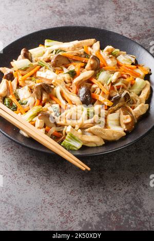 Hachez le poulet frit Suey avec les champignons, le bok choy, l'oignon, les pousses de haricots et les carottes dans une assiette sur la table. Verticale Banque D'Images