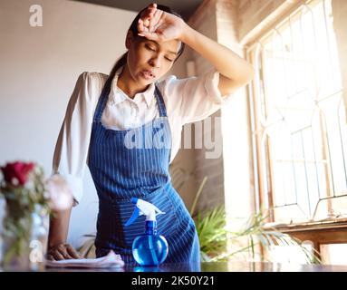 Nettoyage de la maison, l'épuisement et le nettoyant fatigué travaillant dur sur la table sale et les meubles se sentant épuisés. Une femme malheureuse, frustrée et sueur a surtravaillé Banque D'Images