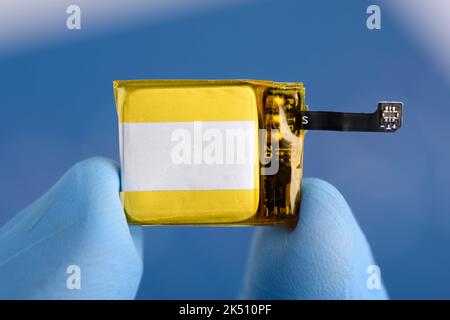 Très petite batterie lithium-ion rechargeable avec connecteur pour montre intelligente ou appareil portable dans les doigts scientifiques en laboratoire Banque D'Images