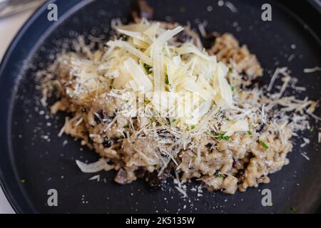 Parmesan râpé sur le risotto aux champignons, sur une assiette noire. Menu végétarien sain, concepts de restaurant chic Banque D'Images