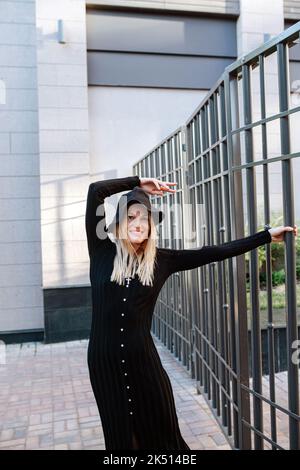 Jeune femme blonde joueur couverte de vêtements noirs accrochés à une clôture en rail Banque D'Images