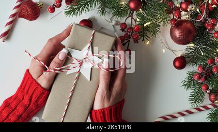 Les femmes tiennent la boîte cadeau de Noël du nouvel an sur fond de branches de sapin, boules rouges, sucettes et guirlandes, vue de dessus, plat Lay.concept celeb Banque D'Images