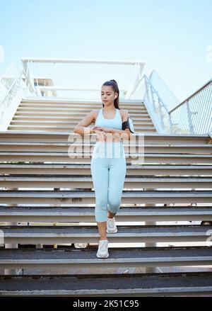 Fitness, montre intelligente et suivi de santé avec femme de sport vérifiant le pouls et la progression pendant l'exercice sur la construction de marches dans une ville. Formation, temps et Banque D'Images