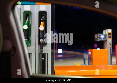 Par la fenêtre de la voiture moderne de pompes à essence avec des buses à la station de remplissage contre le ciel sombre de nuit Banque D'Images