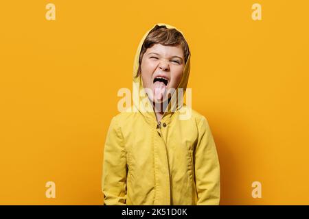 Drôle fille dans l'extérieur coloré montrant la langue et regardant l'appareil-photo tout en faisant grimace sur fond jaune dans studio léger Banque D'Images