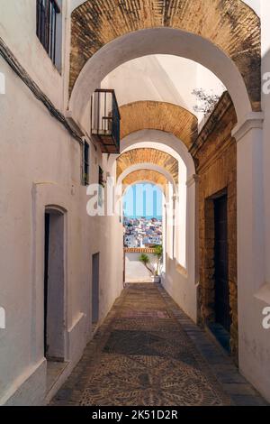 Étroite rue pavée en pierre avec briques et arcs plâtrés blancs au-dessus menant à la vieille ville sous le ciel bleu Banque D'Images