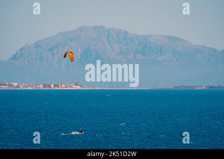 Angle élevé de la personne faisant du kite surf sur les eaux turquoises ondulantes de la mer avec des montagnes floues Banque D'Images