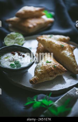 Des triangles de pâte feuilletée sont servis sur une assiette près de la lime pressée et un bol de fromage à la crème sur une drapery sombre Banque D'Images